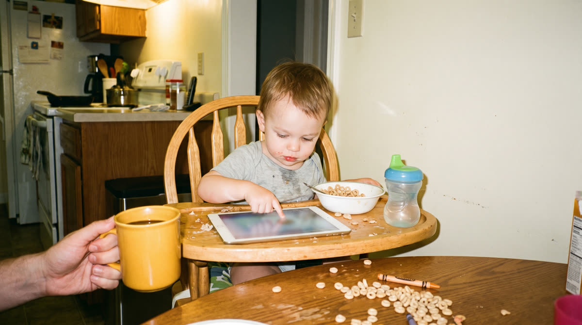 A toddler tapping a tablet at the breakfast table